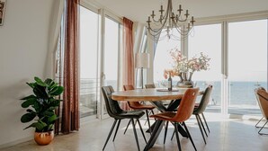 A dining area with a large table, chairs, a chandelier, and a view of the sea. - Apartment in Egmond with Sea Views (Egmond aan zee)