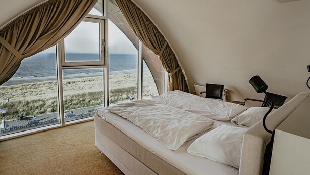 A bedroom with a large window offering a view of the beach and ocean. - Apartment in Egmond with Sea Views (Egmond aan zee)