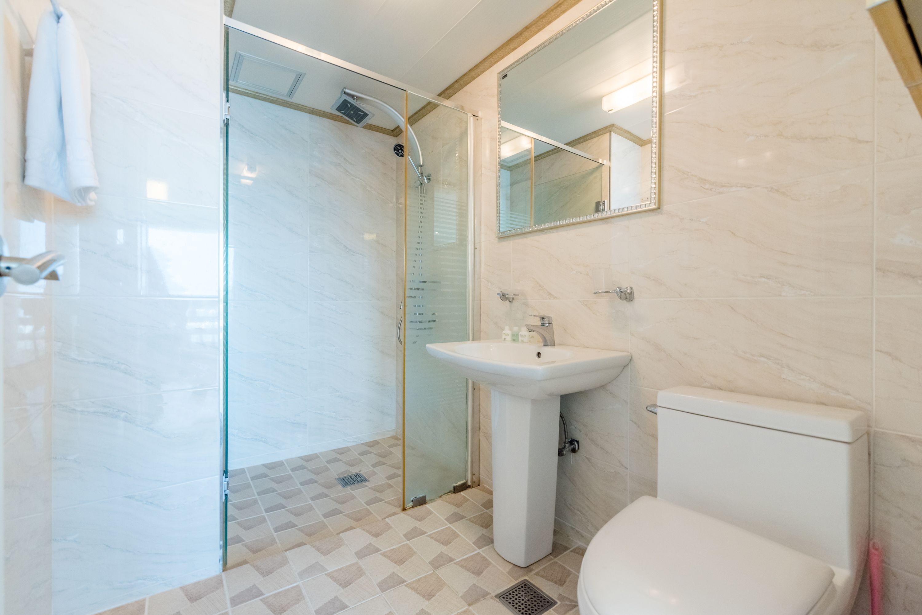 A modern bathroom with a glass-enclosed shower, a pedestal sink, and a toilet.