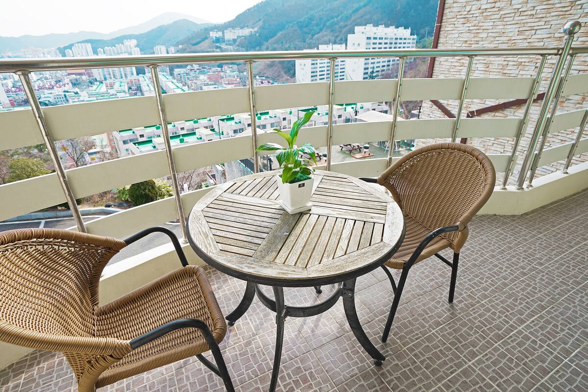 A balcony with wicker chairs and a table, a potted plant, and a city view.