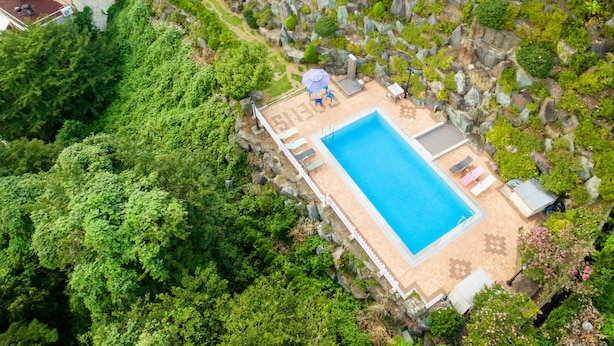 An aerial view of a pool area with a rectangular pool, surrounded by a white fence, and lush greenery.