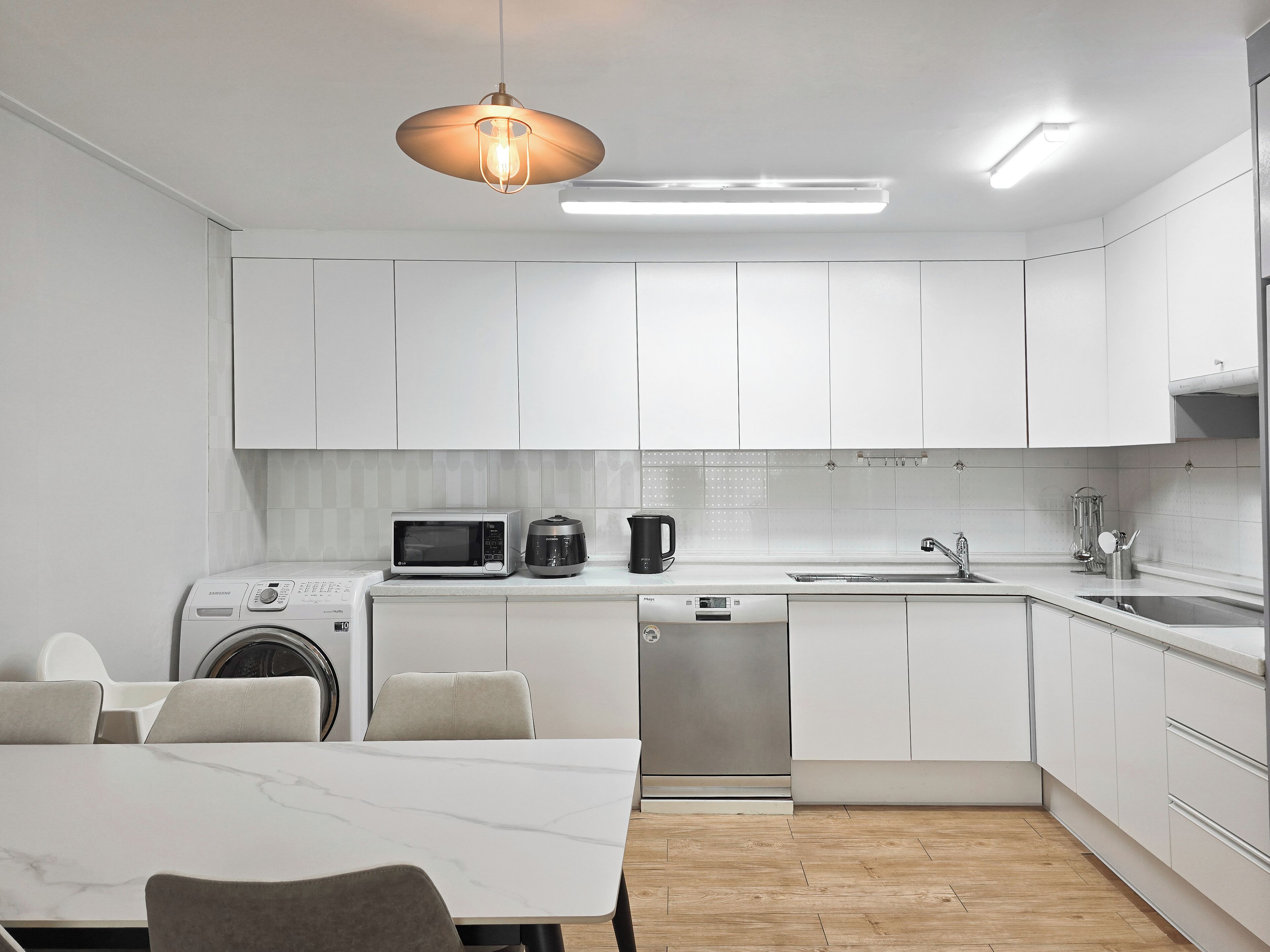 Una cocina moderna con armarios blancos, microondas, cafetera y lavavajillas.