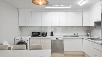 Una cocina moderna con armarios blancos, microondas, cafetera y lavavajillas.