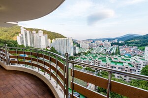 Un balcón con vista a un paisaje urbano, que incluye edificios altos y una colina verde al fondo.