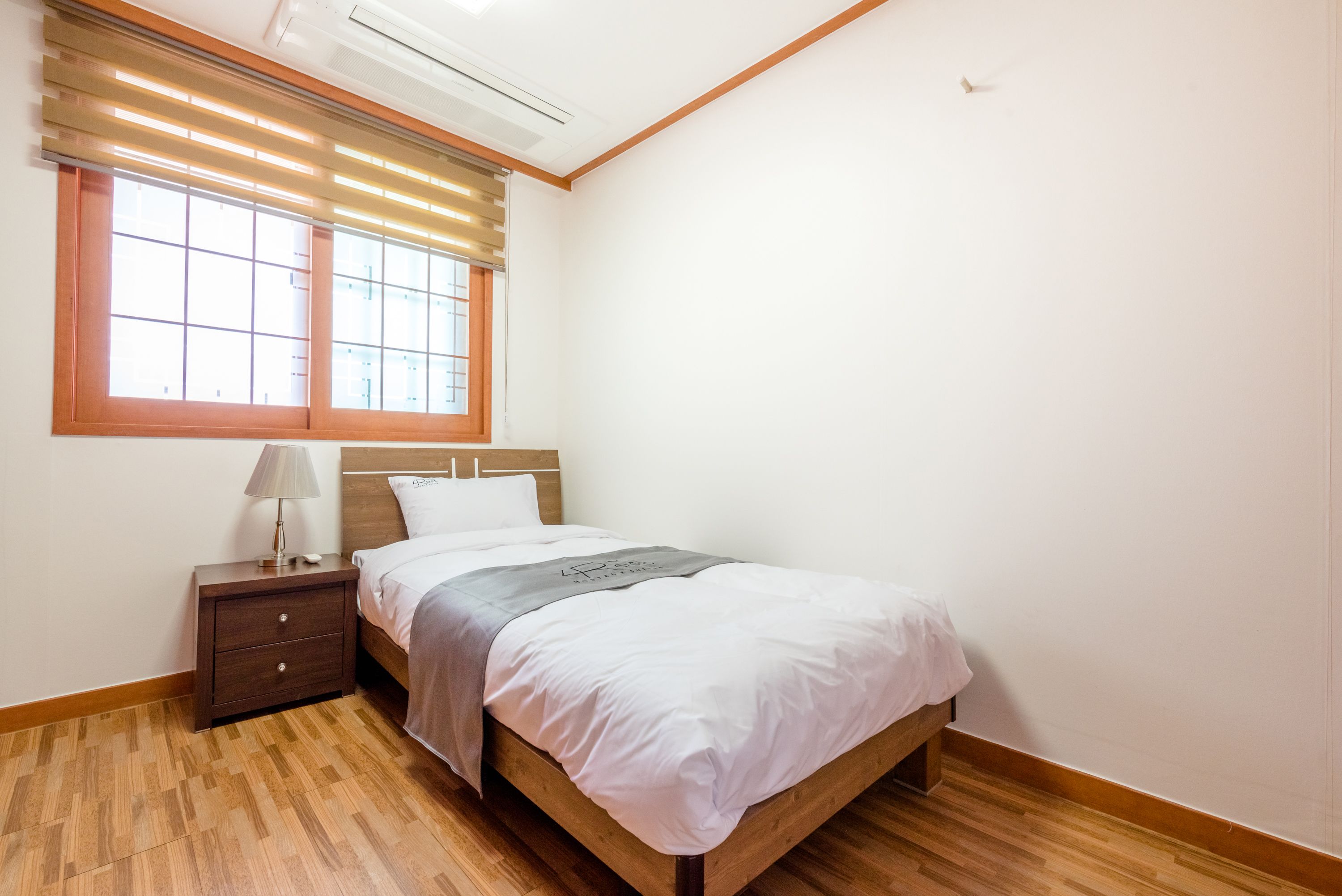 Una camera da letto con un letto in legno, un comodino con una lampada e una finestra con persiane.