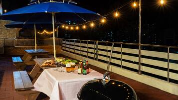 Un área de comedor al aire libre con mesas de picnic, una parrilla y luces colgantes.