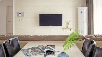 Una sala moderna con una televisión de pantalla plana montada en la pared, un sofá, una mesa de comedor con sillas y una pequeña planta sobre la mesa.