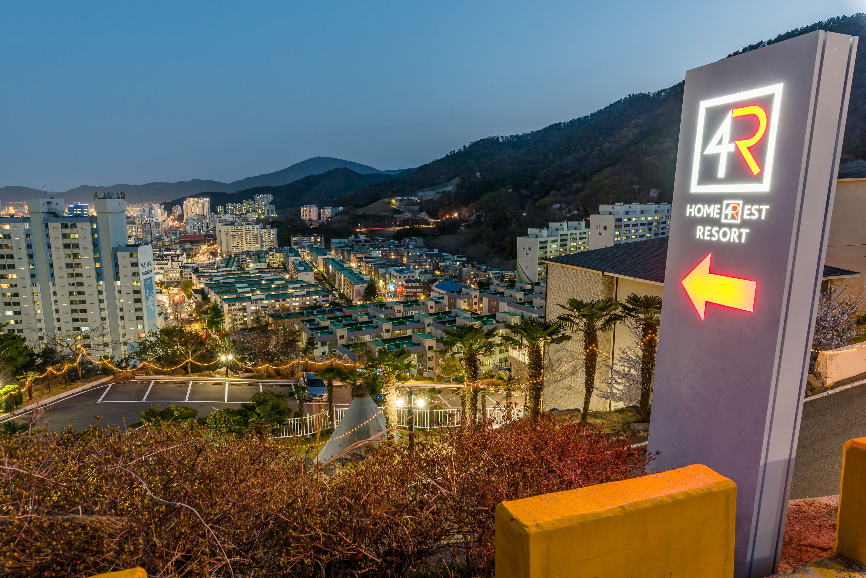A sign for Home Rest Resort with an arrow pointing left, surrounded by buildings and a mountainous backdrop.
