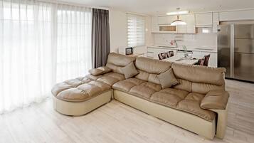 A modern living room with a large L-shaped sectional sofa, a dining table with chairs, and a kitchen area with a refrigerator and microwave.