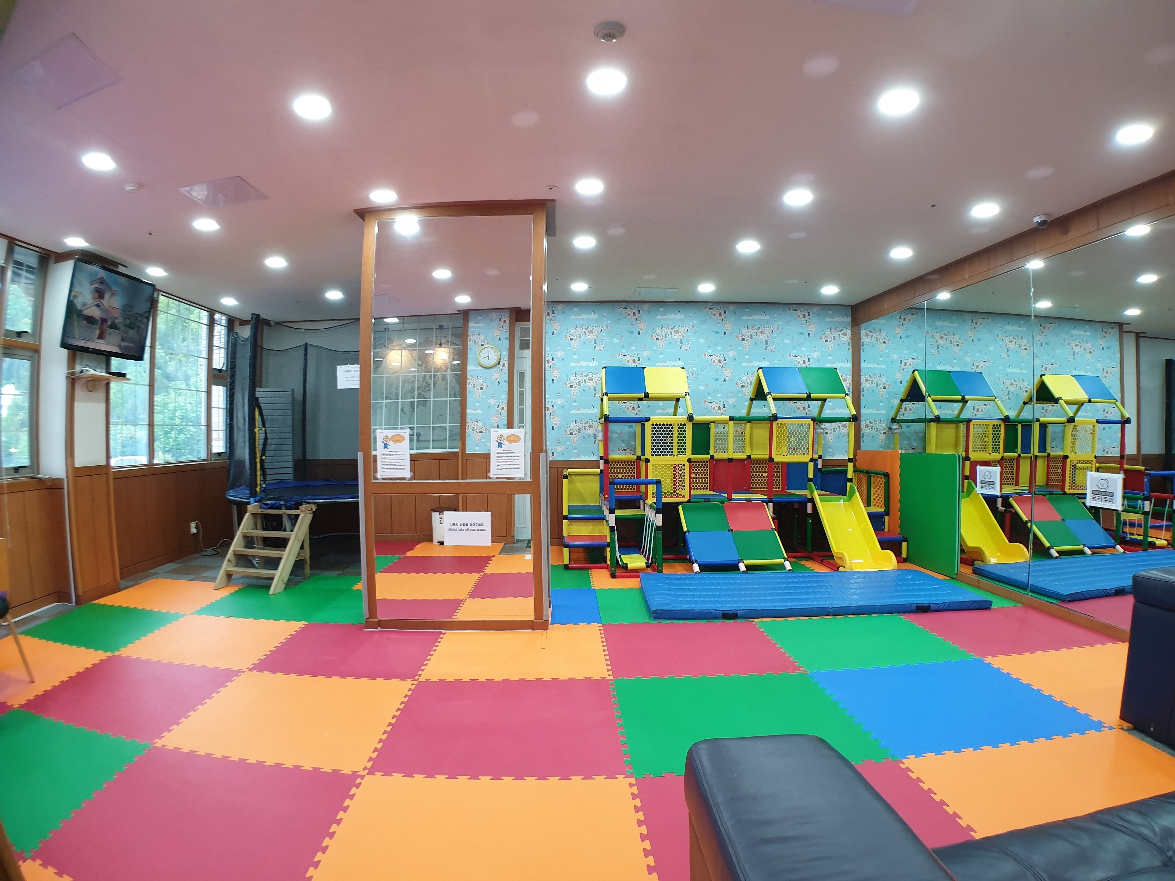A play area with colorful padded flooring, play structures, and a mirrored wall.