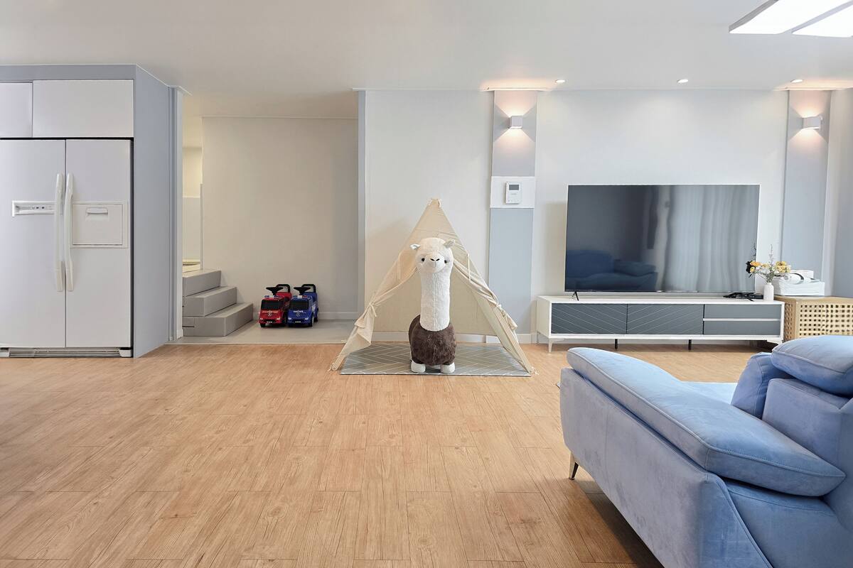 A modern living room with a sofa, a TV, and a tent-like structure with a stuffed animal.