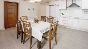 Comedor con mesa y sillas de madera, salpicadero de azulejos blancos y extractor de acero inoxidable sobre la estufa.