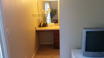 A bathroom with a toilet, sink, mirror, and a television on a stand.