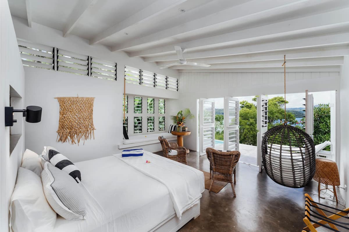 Un dormitorio amplio con una cama grande, una silla colgante y vistas a la vegetación.
