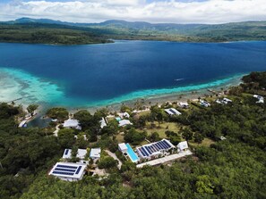 Luftaufnahme einer Küstenimmobilie mit mehreren Gebäuden, einem Swimmingpool und Solaranlagen.