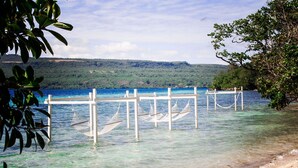 Ein Strand mit klarem Wasser, einer Holzsteganlage und einem grünen Hügel in der Ferne.