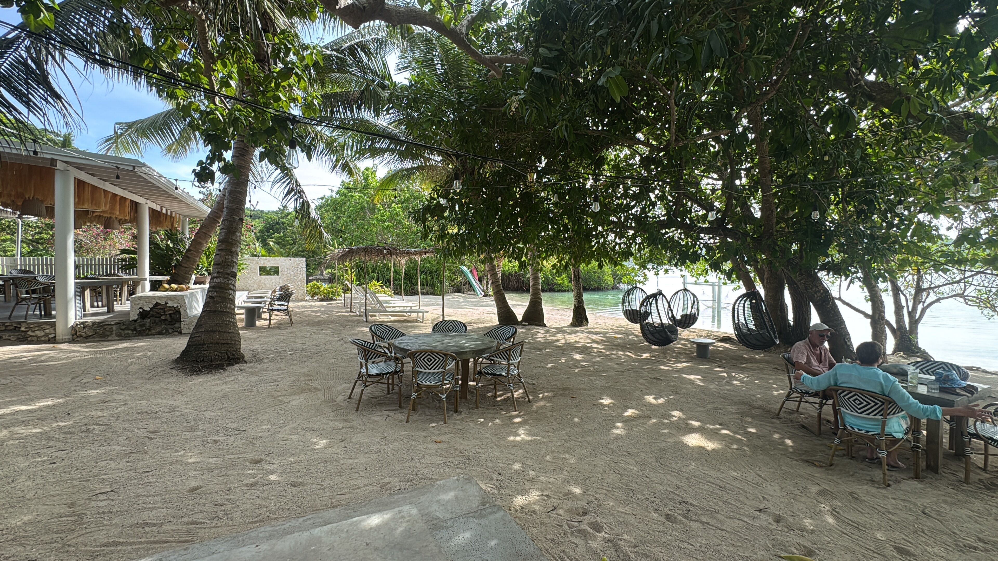 An outdoor seating area with tables and chairs, surrounded by trees and a view of the water.