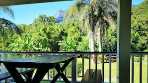 A wooden deck with a picnic table and bench, surrounded by lush greenery and a mountain in the background. - Cottage HANA MANA (Yakushima)