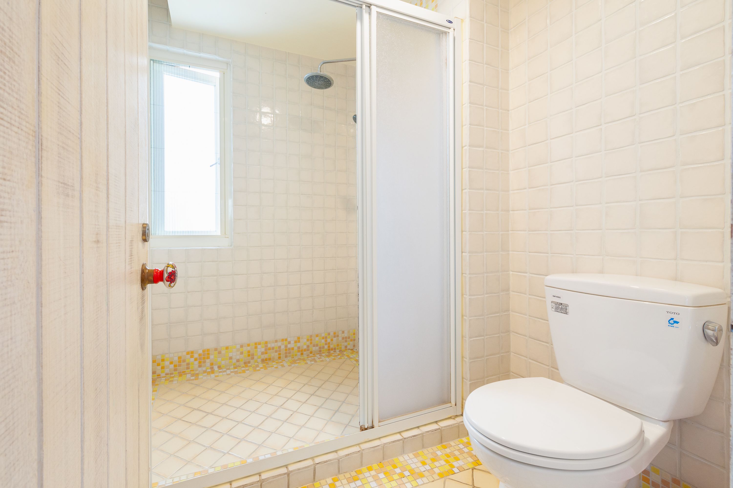A bathroom with a shower, toilet, and a window.
