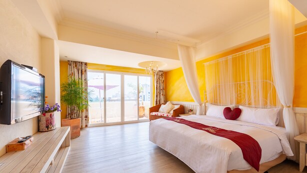 A spacious bedroom with a large bed, a television, and a balcony with curtains. - Mong Shan Homestay (Hengchun)