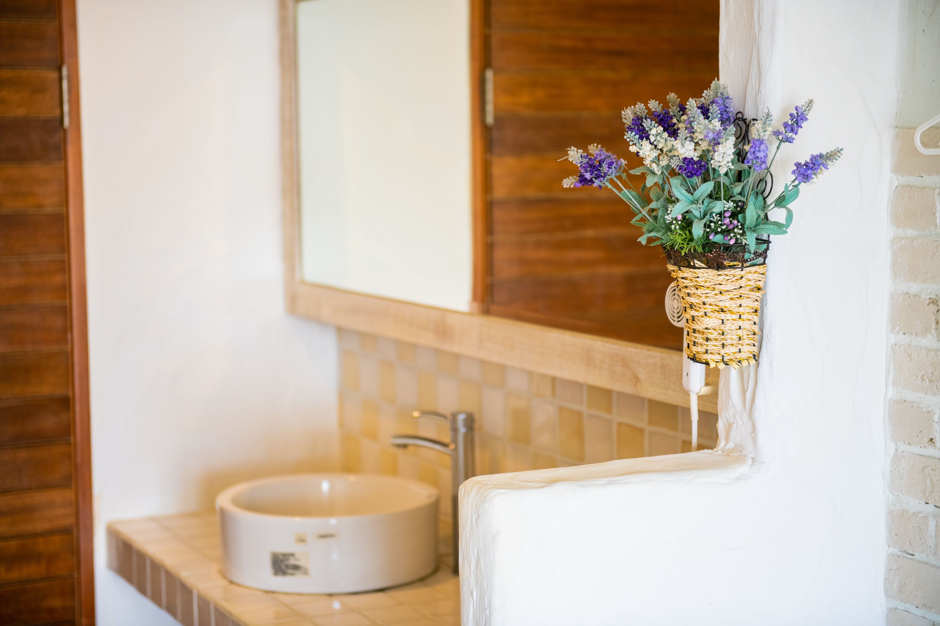 A bathroom with a round sink, a mirror above it, and a wicker basket with flowers on the wall.