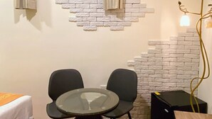 A small room with a brick wall, a window with curtains, a round table with chairs, a bed, and a black speaker. - Mong Shan Homestay (Hengchun)