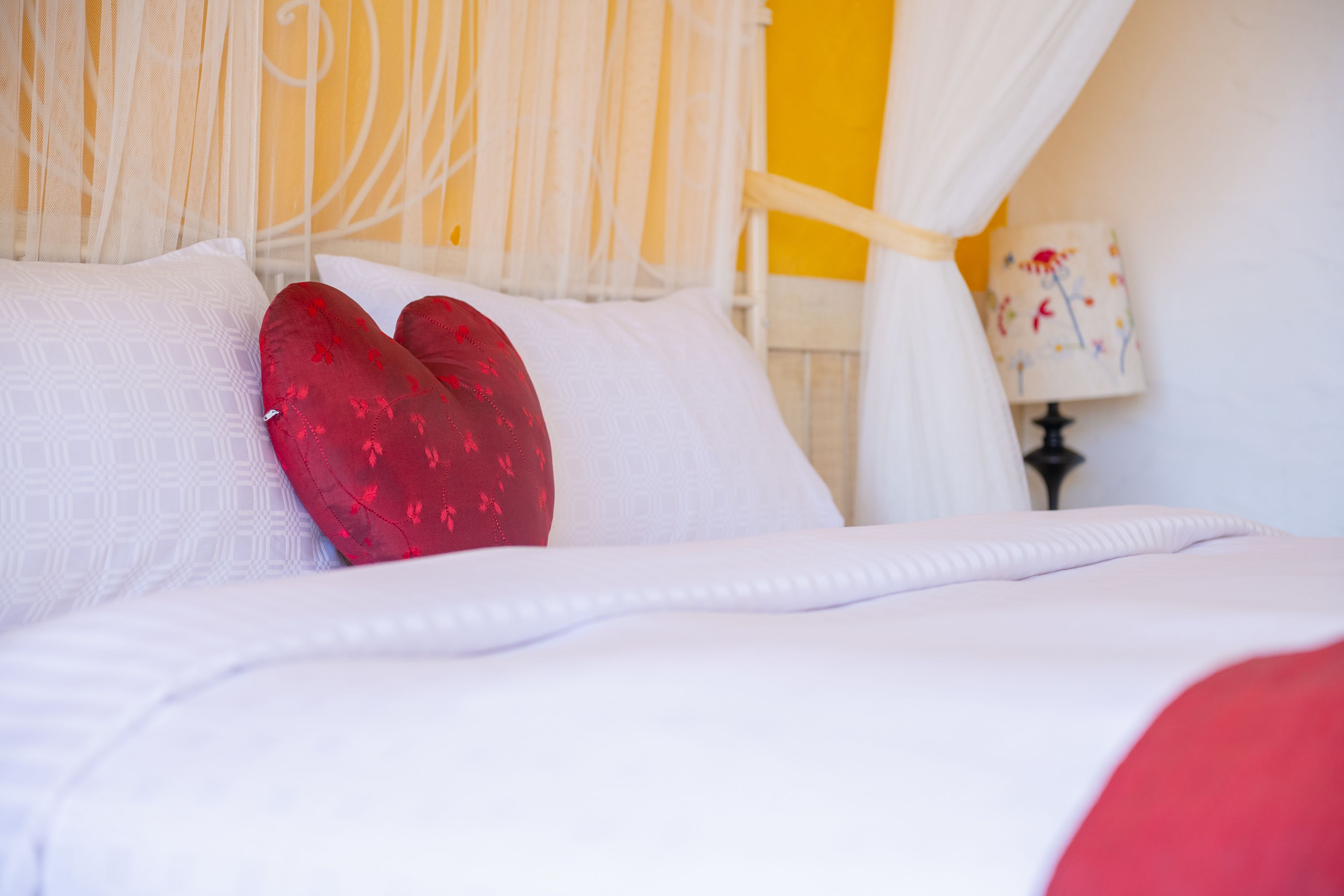 A neatly made bed with white and red pillows, a white bedspread, and a yellow wall in the background.