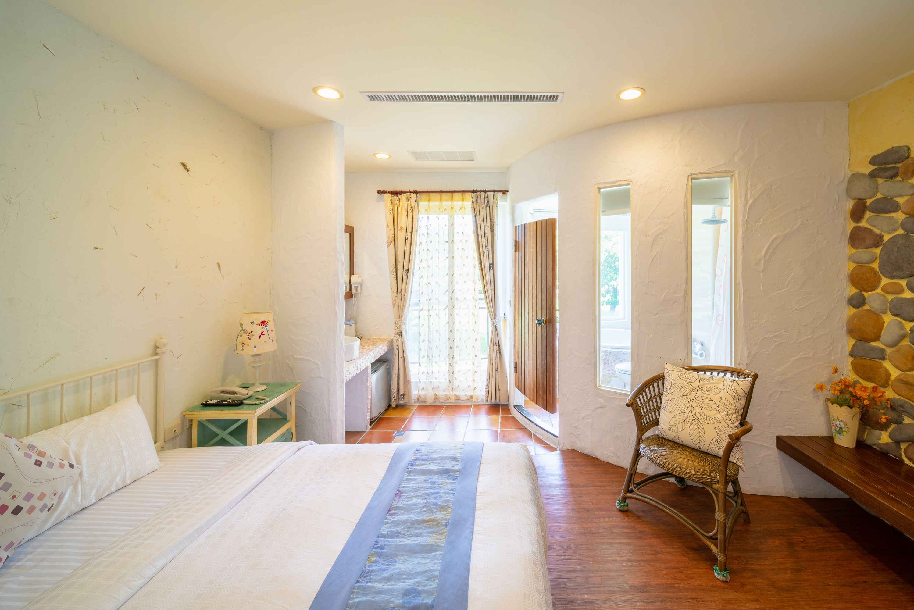 A bedroom with a bed, a chair, a small table, and a window with curtains.