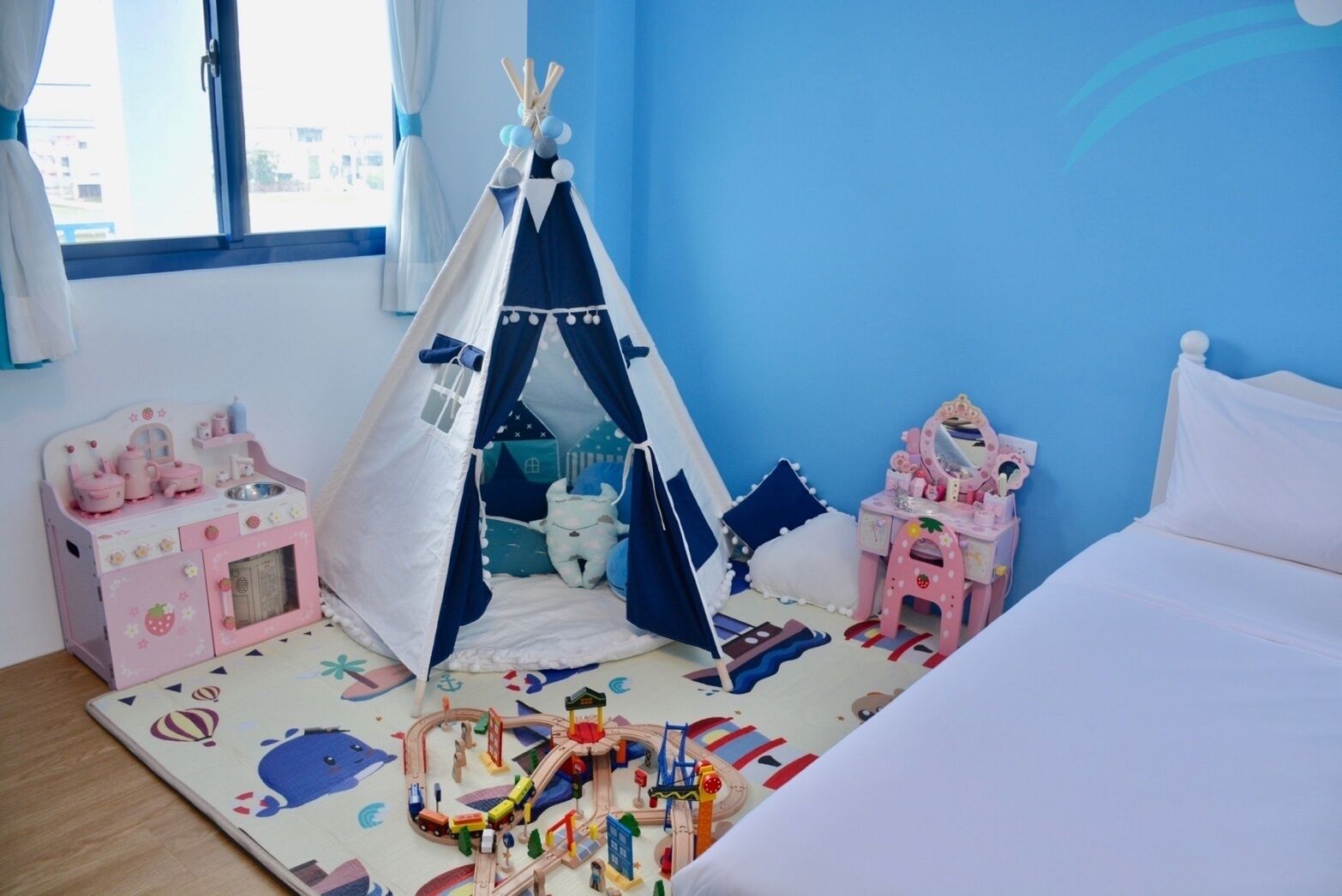 Een kinderkamer met een tent, een roze keukentje en een bed.