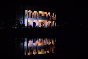 Um edifício de dois andares com janelas em arco e varandas, refletindo na água em frente.