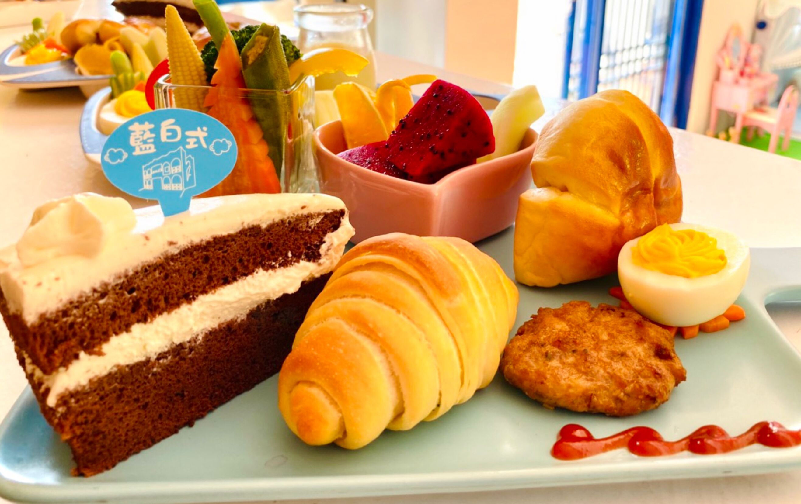 A plate with a slice of cake, croissants, a boiled egg, and a small dish of fruit.