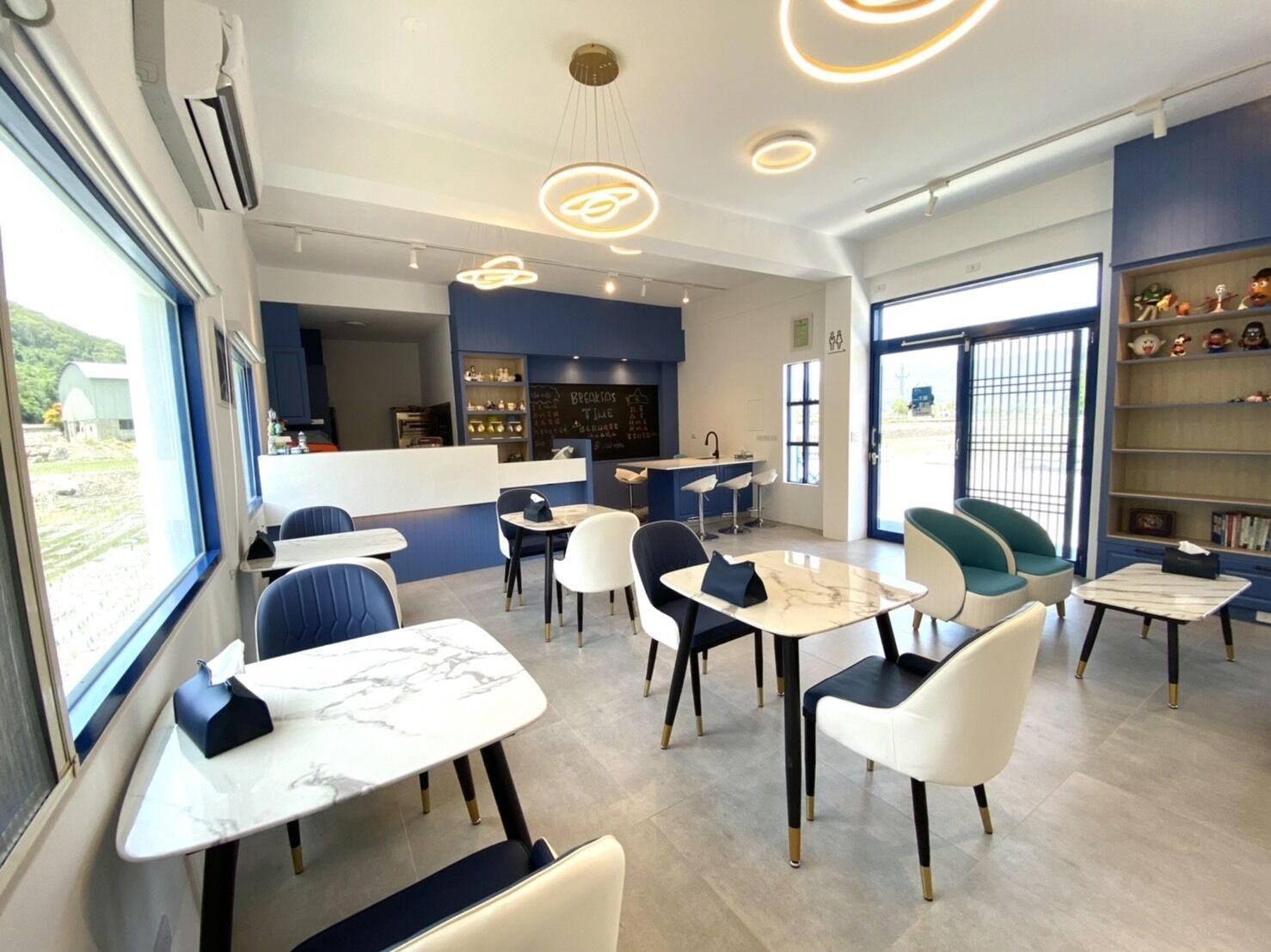 A modern cafe with marble tables and chairs, a counter with a chalkboard menu, and a view of the outdoors.