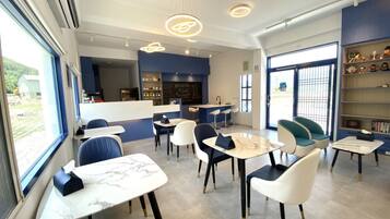 A modern cafe with marble tables and chairs, a counter with a chalkboard menu, and a view of the outdoors.