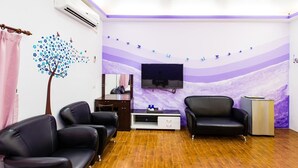 A room with a TV mounted on the wall, two black leather sofas, a wooden cabinet, and a wall mural with a tree and butterflies. - Kenting Star Inn (Hengchun)