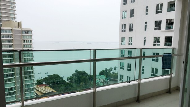 Een balkon met glazen hekwerk, met uitzicht op water en gebouwen.
