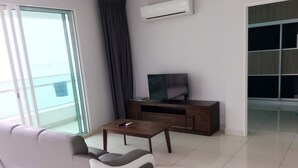 Een moderne woonkamer met een bank, een salontafel, een televisie op een houten kast en een schuifdeur naar een balkon.