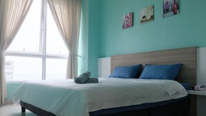 Een opgemaakt bed met een witte dekbedovertrek en blauwe kussens, een houten hoofdbord en een raam met gordijnen.