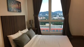 Une chambre d’hôtel avec un grand lit, une table de chevet avec une lampe, un tableau au mur et une vue sur le paysage urbain par la fenêtre.