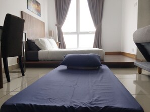 Quarto com cama, cadeira e janela com cortinas.