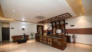 Zona de recepción de un hotel con un mostrador de madera, un sofá de cuero marrón y una planta en maceta.
