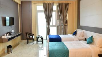A hotel room with two beds, a TV mounted on the wall, a small table with a chair, and a window with curtains.