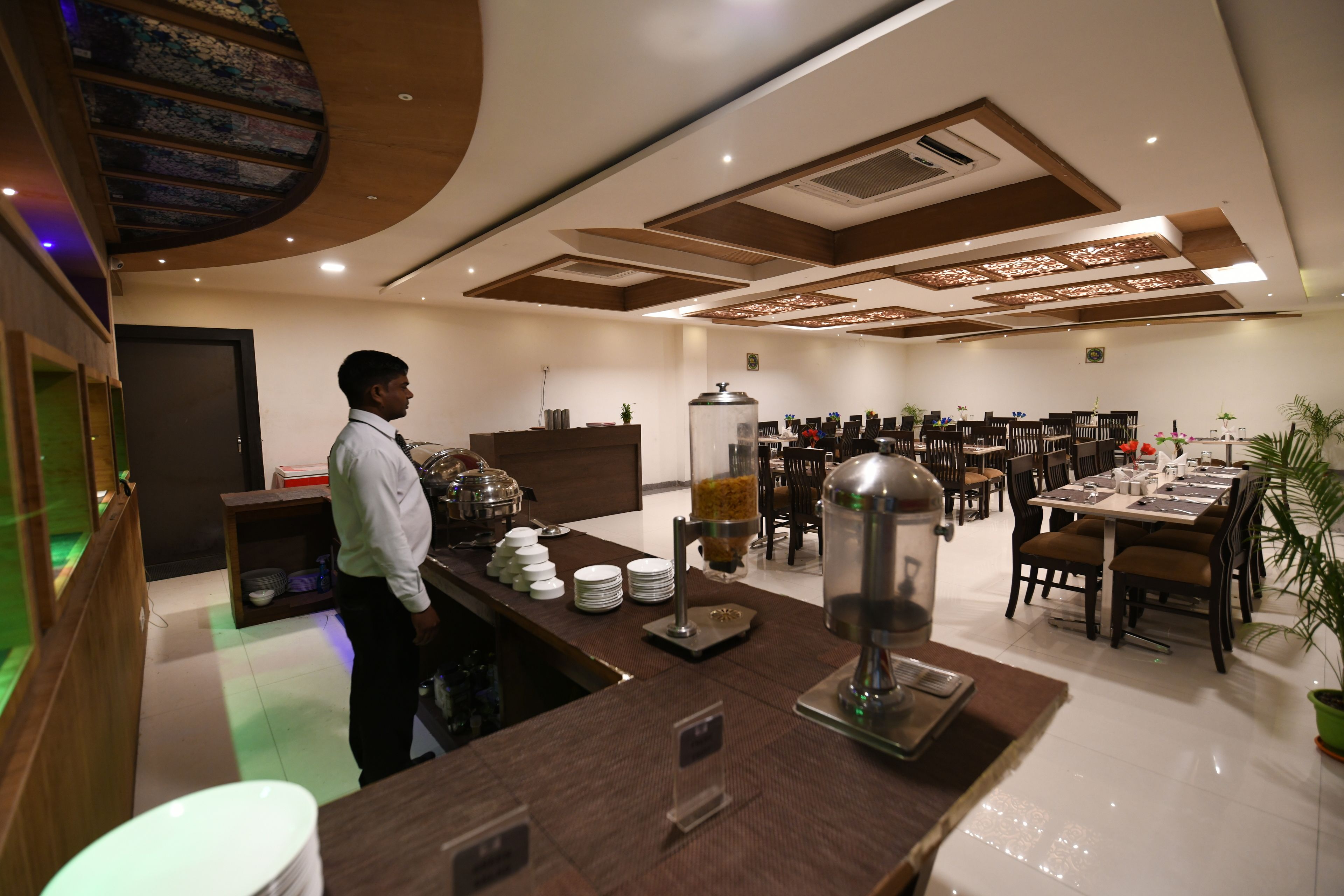Espaço de refeições de hotel com serviço de buffet, várias mesas e cadeiras.