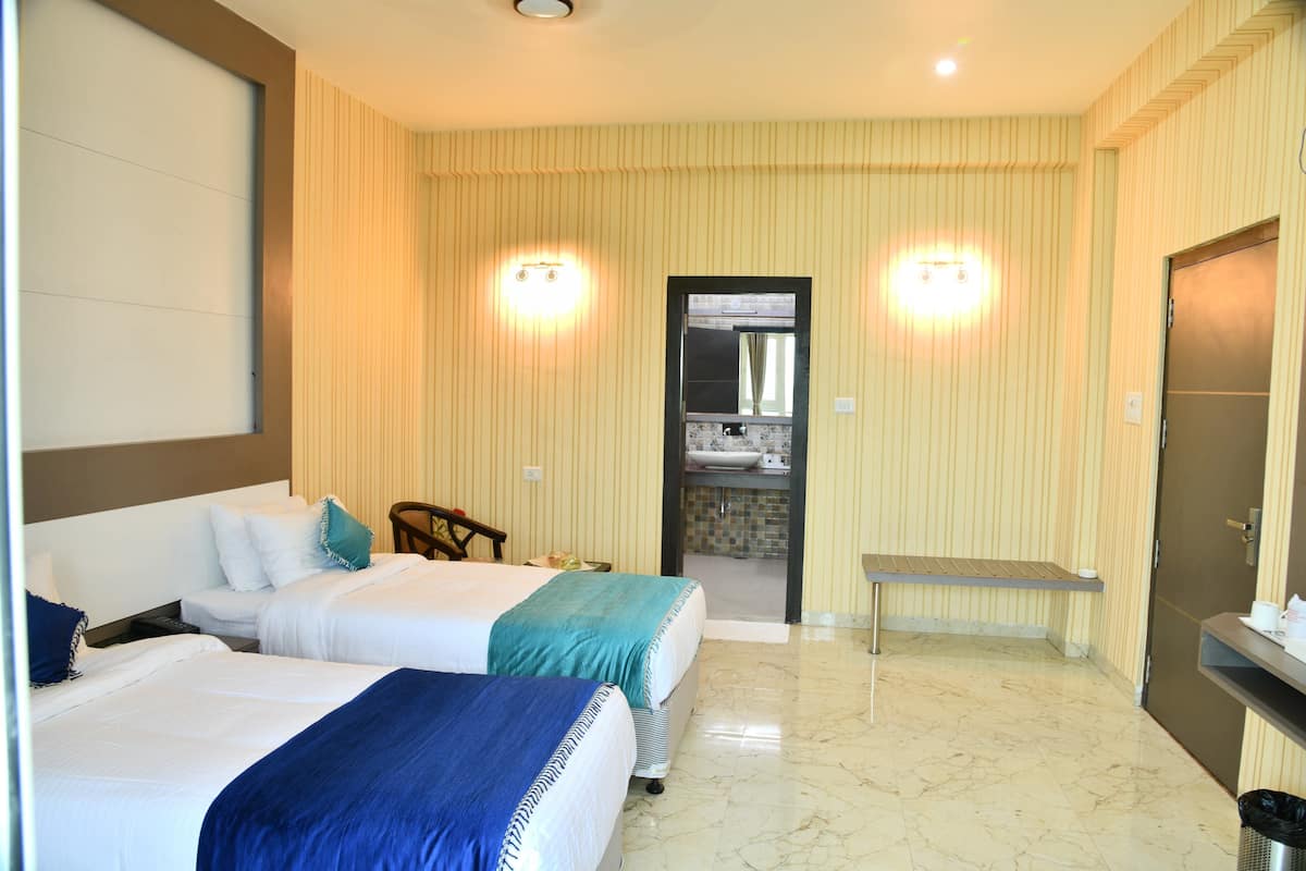 A hotel room with two beds, a small table, a bench, a mirror, and a door leading to a bathroom.