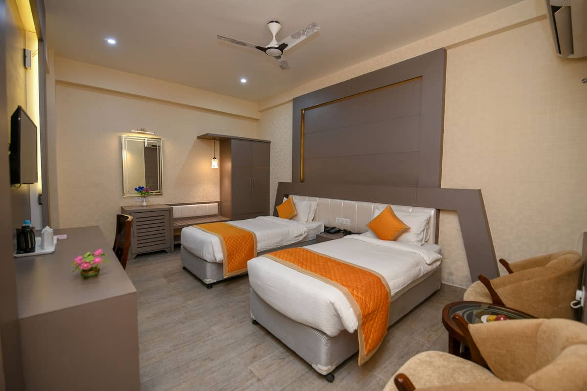 A hotel room with two beds, a desk, a chair, a TV, and a ceiling fan.