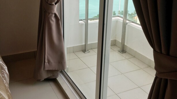 A room with a large window, curtains, and a view of a balcony with a railing and a body of water. - Mansion One Bedroom Suite (George Town)