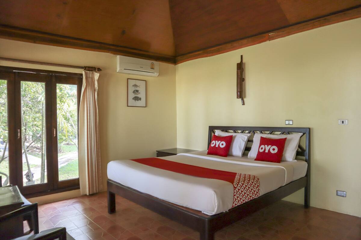A hotel room with a bed, a nightstand, a window with curtains, and an air conditioning unit.