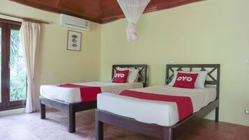 A room with two beds, each with a red 'OYO' pillow, a mosquito net above, and an air conditioner on the wall.