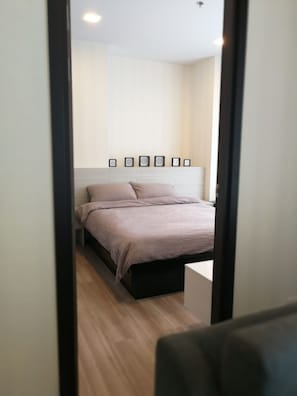 A bedroom with a bed, a bedside table, and a wall-mounted shelf with framed pictures.