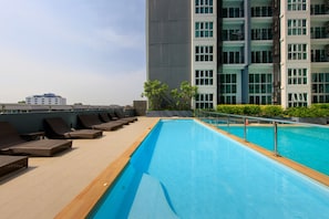 A rooftop swimming pool with lounge chairs and a view of a high-rise building.