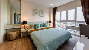 Een moderne hotelkamer met een groot bed, een bureau, een stoel en uitzicht op de stad door grote ramen.